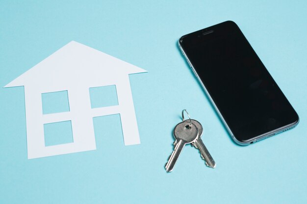 Бумажный вырез дома и ключи с мобильным телефоном на синем фоне