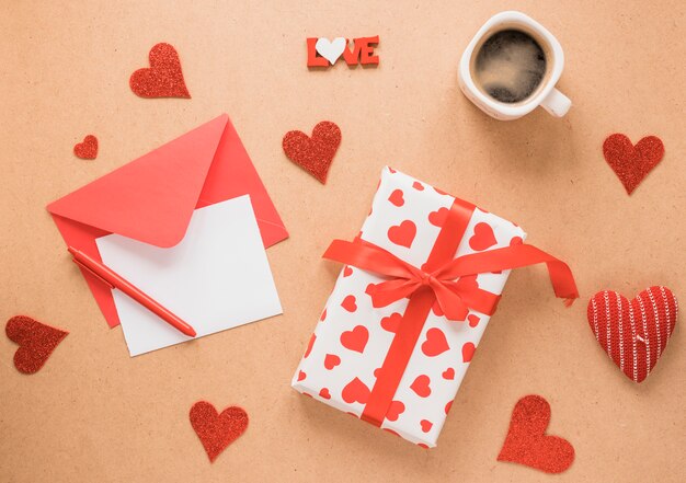 Бумага на конверте возле ручки, подарок, чашка напитка и украшение сердца