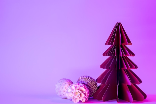 Paper fir tree with christmas balls on blue background with neon light