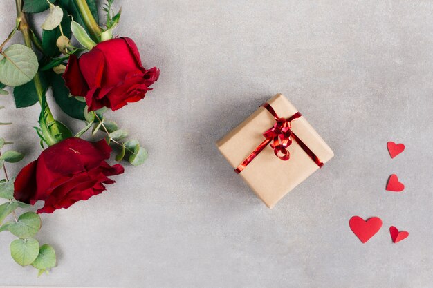 Paper hearts near present box in wrap and flowers