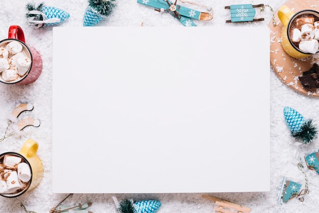 Paper between mugs with marshmallows and Christmas toys on snow 