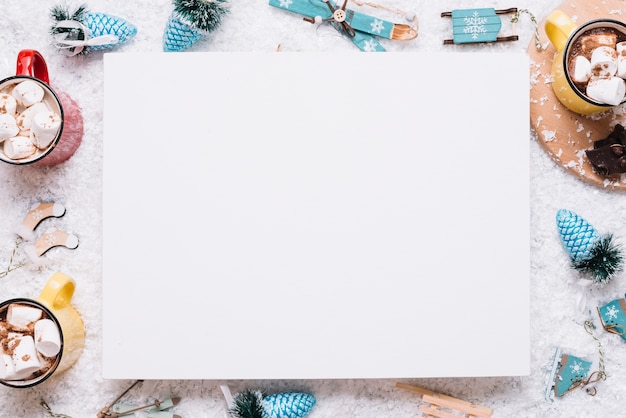 Paper between mugs with marshmallows and Christmas toys on snow 