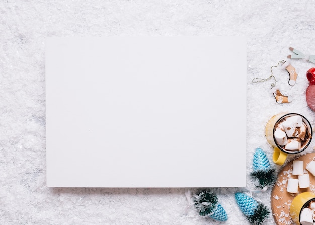 Free photo paper near mugs with marshmallows and christmas toys on snow