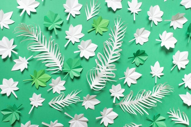 Paper season composition with green white maple leaves and paper feathers on green background.