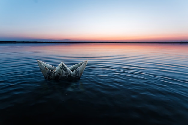 A paper ship made from banknotes, made from dollars, floats in the water against the backdrop of a beautiful sunset. origami from money, financial business model, copy space.