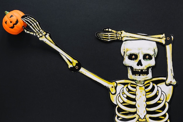 Paper skeleton with pumpkin on black background