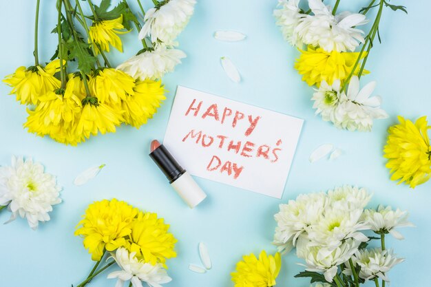 Paper with happy Mothers day words near lipstick and bunches of fresh flowers