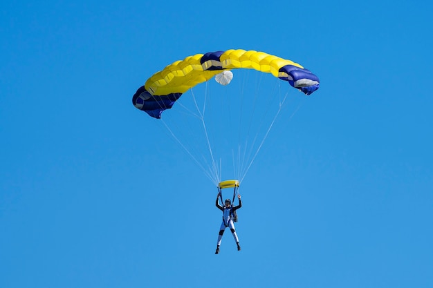 青い​空​を​背景​に​黄色​と​青​の​パラシュート​を​持つ​落下傘兵
