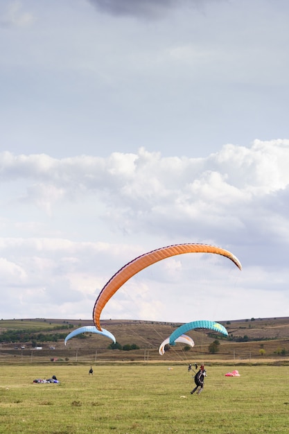 Paragliders silhouette flying over beautiful green landscape under blue sky with clouds.