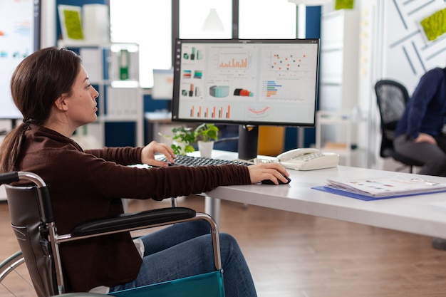 Paralyzed businesswoman in wheelchair typing marketing strategy working at company