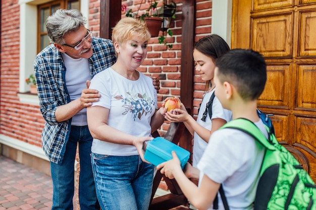 Parents  are going to send their children to the school bus. give eat for them. Kids shoulder schoolbag.