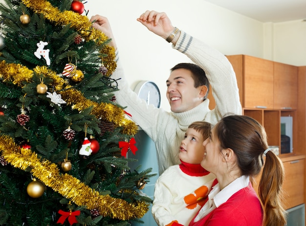 Родители и девочка, украшающие елку