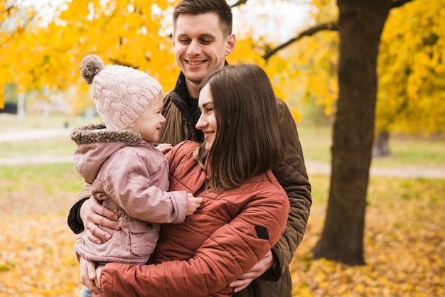 Parents and daughter embracing in autumn park smiling