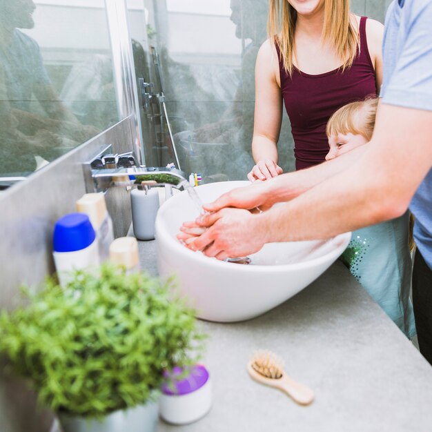 Parents helping daughter to wash hands