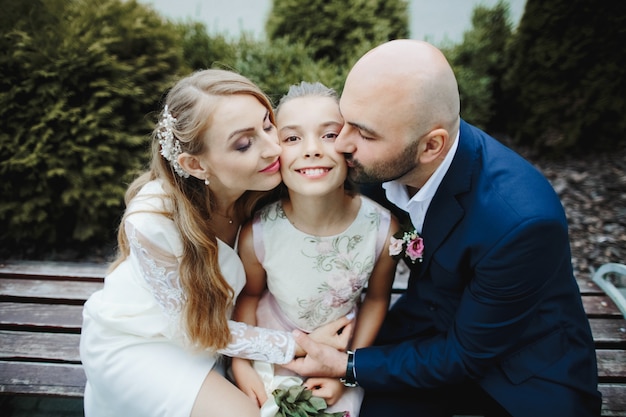 Parents kiss their daughter at her cheeks