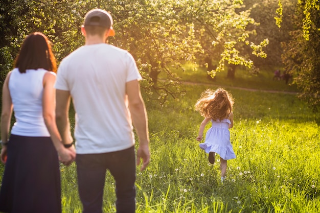 Бесплатное фото Родители, смотрящие на свою девочку, бегущую в парке