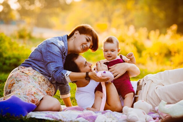 Parents play with little girl on the blanket in rays of evening sun