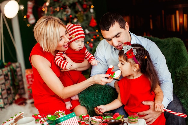 Parents play with their two children at the table before green Christmas tree