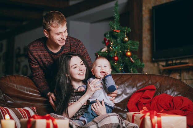 Parents smiling looking at their baby with hand in mouth and with christmas gifts