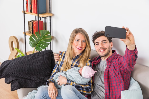 Free photo parents taking selfie with baby on couch