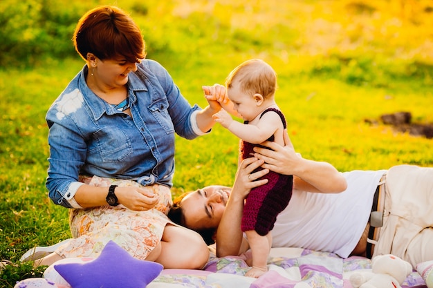 Parents and their little daughter lie on the blanket on green lawn 