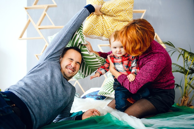 Родители и их маленькая дочь играют с подушками на полу