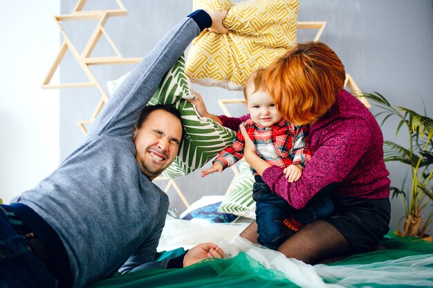 Parents and their little daughter play with pillows on the floor 