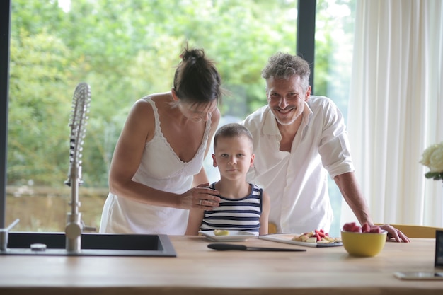 Parents and their son standing against the kitchen counter with food on it under the sunlight