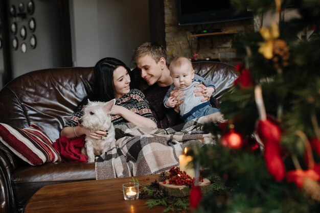 Parents with a baby at christmas and a dog sitting on the couch