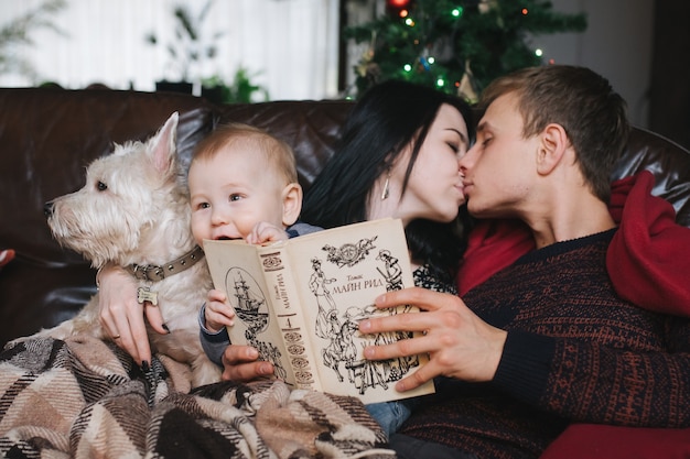 クリスマスで赤ちゃんとソファに座って犬を持つ親