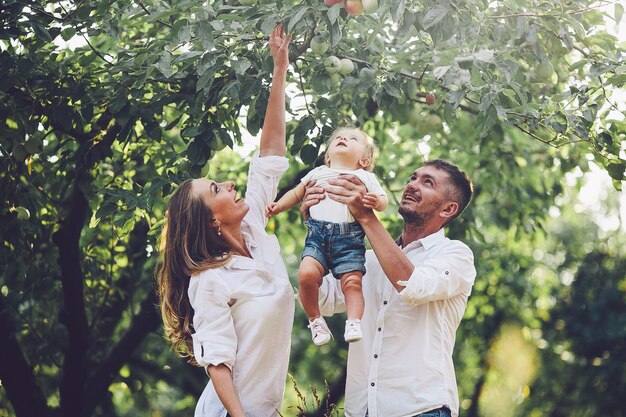 Parents with baby enjoying picnic on a farm with apple and cherry trees.