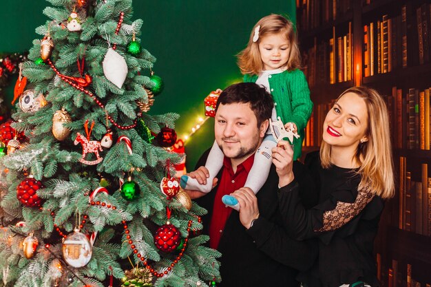 Parents with little blonde girl pose before a Christmas tree in the room