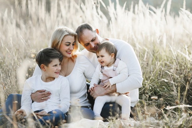 Parents with their two children sit on the meadow and are looking at the little cute girl