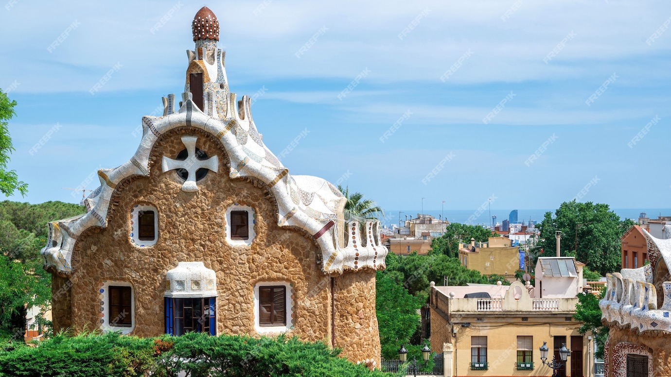 A whimsical building with mosaic details and a unique rooftop design in a lush park, overlooking a cityscape under a blue sky.