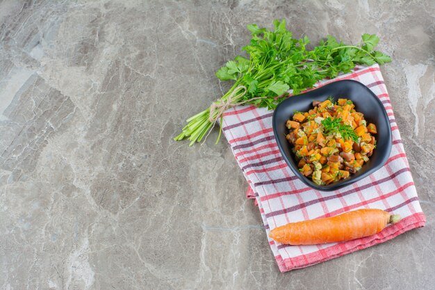 Петрушка, морковь и запеченные бобы в миске на кухонном полотенце на мраморном столе.