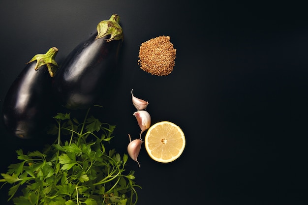 Parsley, garlic, lemon, sesame seeds and two fresh eggplants isolated on black