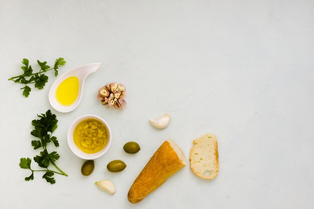 Parsley leaves; olive oil; garlic and bread on white textured backdrop