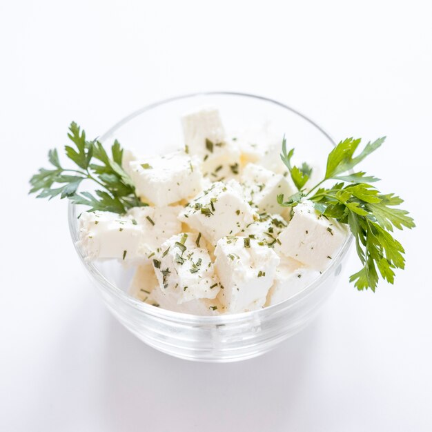 Parsley with cheese cubes in the glass bowl against white background