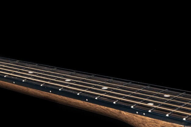 Part of an acoustic guitar, guitar fretboard on a black background.