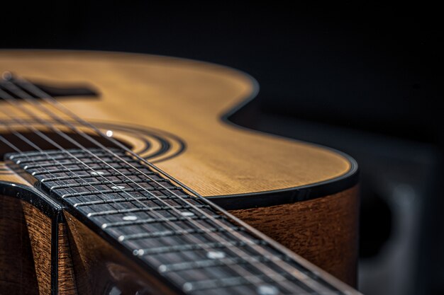 Часть акустической гитары, гриф гитары со струнами на черном фоне с бликами.