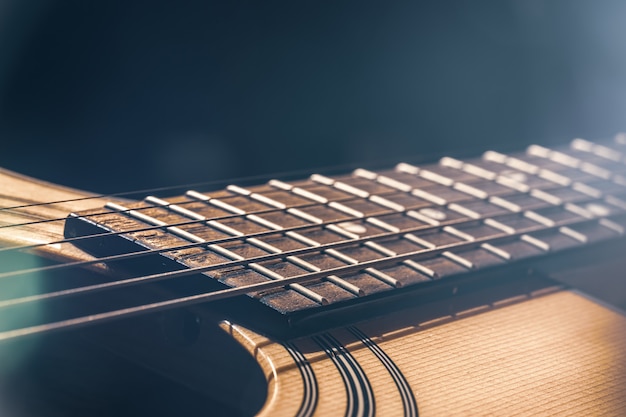 アコースティックギターの一部であり、ハイライトのある黒い背景に弦が付いたギター指板。