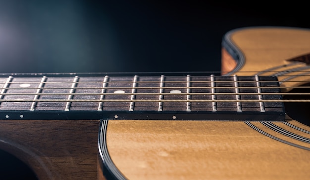 Part of an acoustic guitar, guitar fretboard with strings on a black background.