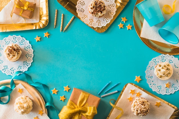 Party accessories with muffins and birthday gifts on turquoise backdrop