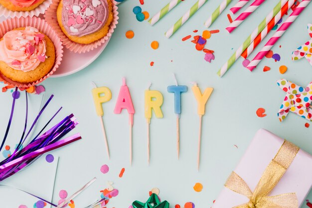 カップケーキに囲まれたパーティーキャンドル。ストロー支柱と青い背景に紙吹雪