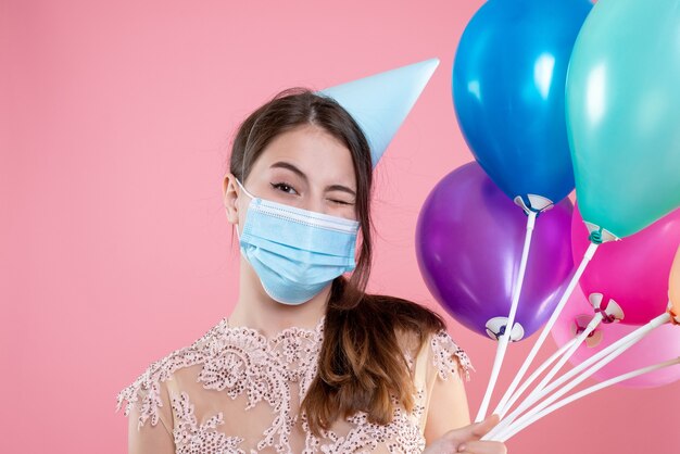 party girl with crown and mask blinking eye holding balloons on pink