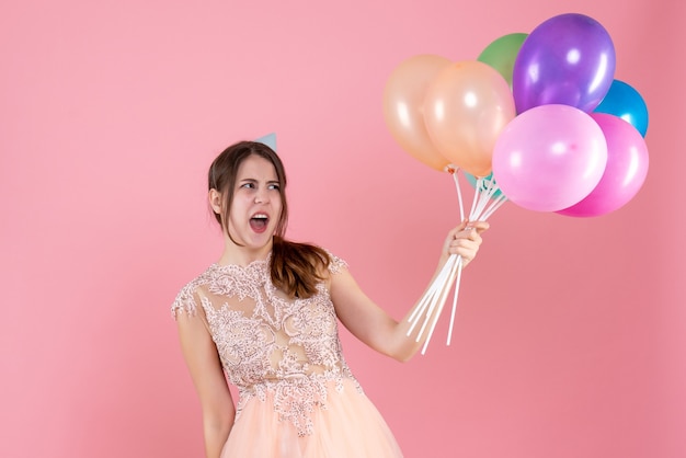 party girl with party cap holding balloons shouting on pink