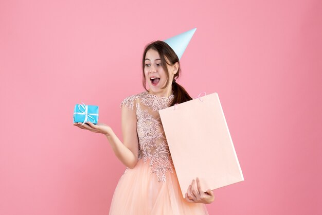 party girl with party cap holding gift and shopping bag on pink