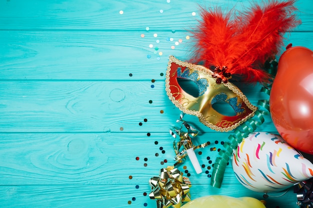 Party hat; balloon with confetti and golden masquerade carnival mask on wooden table