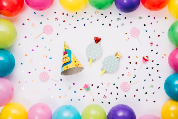 Party hat and horn blower decorated with colorful balloons and confetti isolated on white backdrop