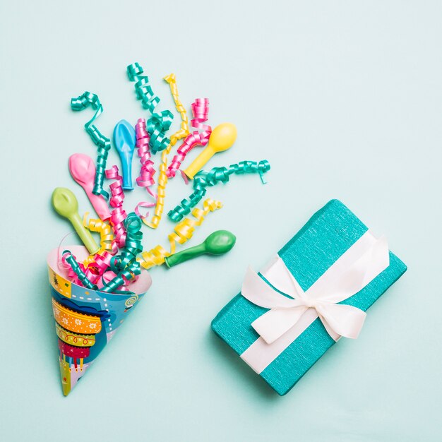 Party hat with streamers; balloons and wrapped present on blue backdrop